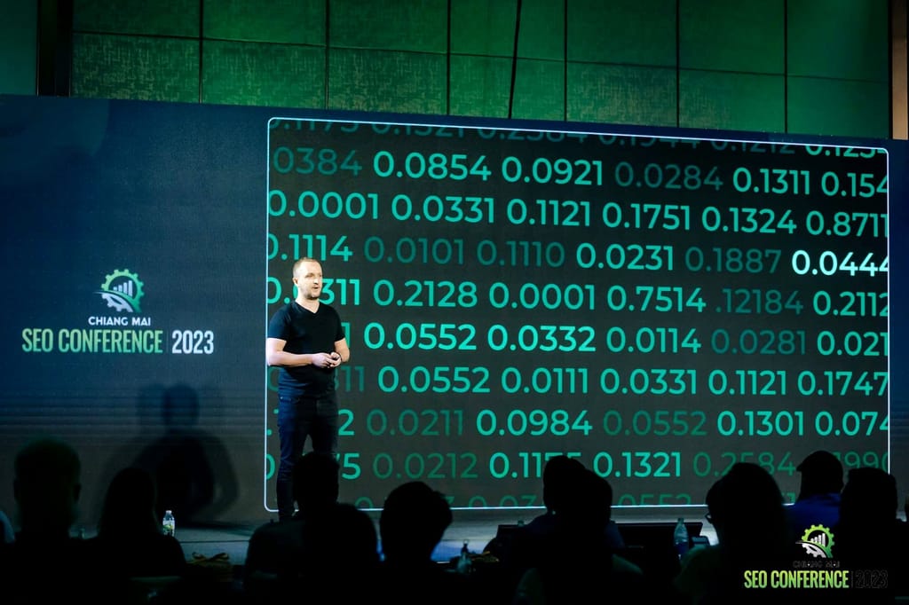 Robert Niechciał na scenie Chiang Mai SEO Conference 2023, po lewej logo konferencji, za nim zielony slajd pełen liczb