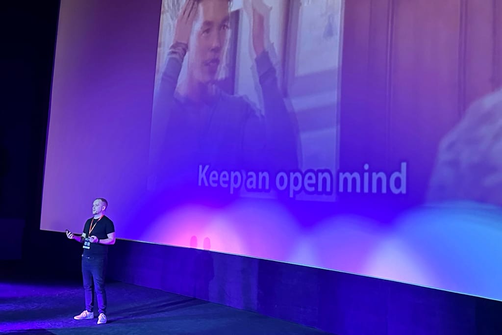 Robert Niechciał na scenie przed wielkim kinowym ekranem, za nim slajd „Keep an open mind”