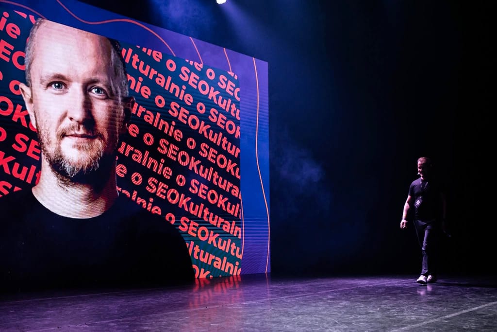 Robert Niechciał idzie przez scenę Kulturalnie o SEO, za nim jego portret na ekranie LED