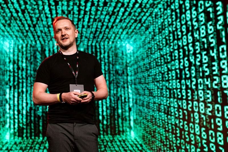 Robert Niechciał na scenie Kulturalnie o SEO 2026 na tle zielonej ściany cyfr w stylu matrixa
