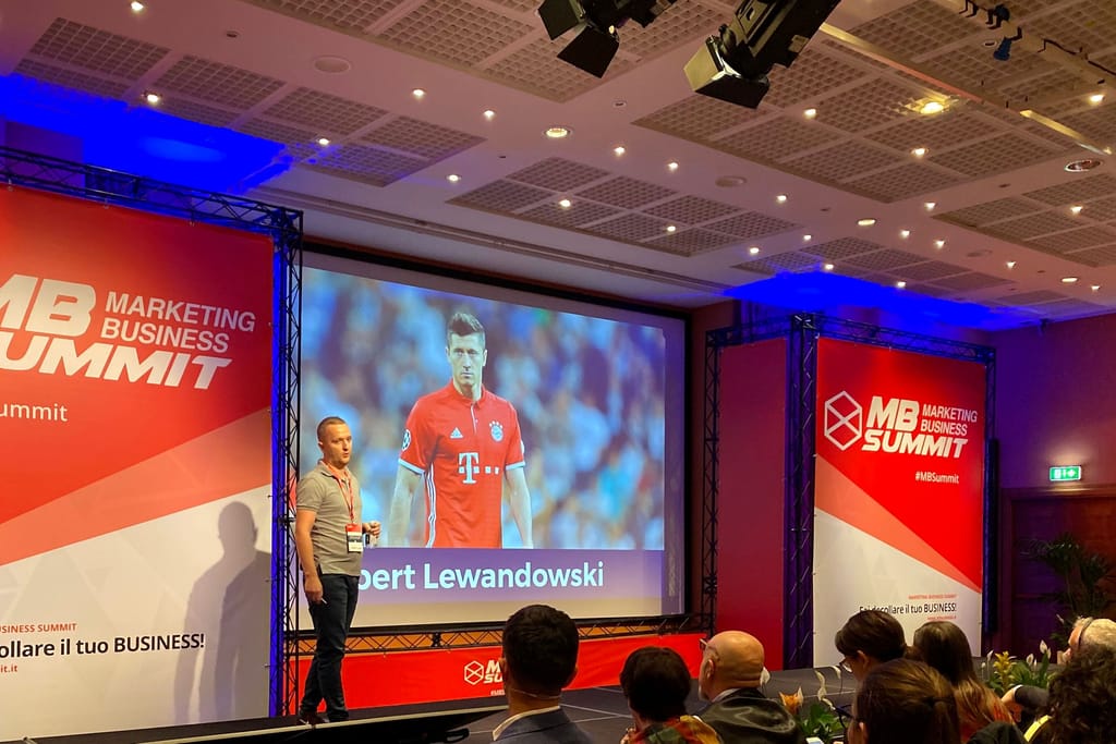 Robert Niechciał na scenie Marketing Business Summit we Włoszech, między czerwonymi banerami #MBSummit