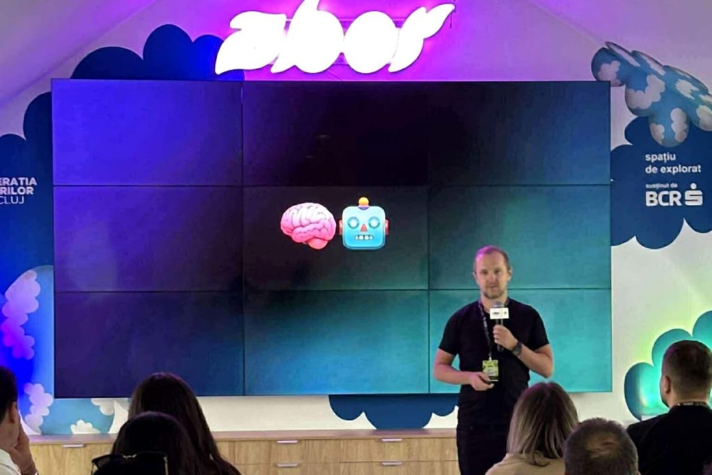 Robert Niechciał mówi do mikrofonu przed ścianą wideo z emoji mózgu i robota na Search Evolution Summit 2025 w Kluż-Napoce, publiczność widziana od tyłu