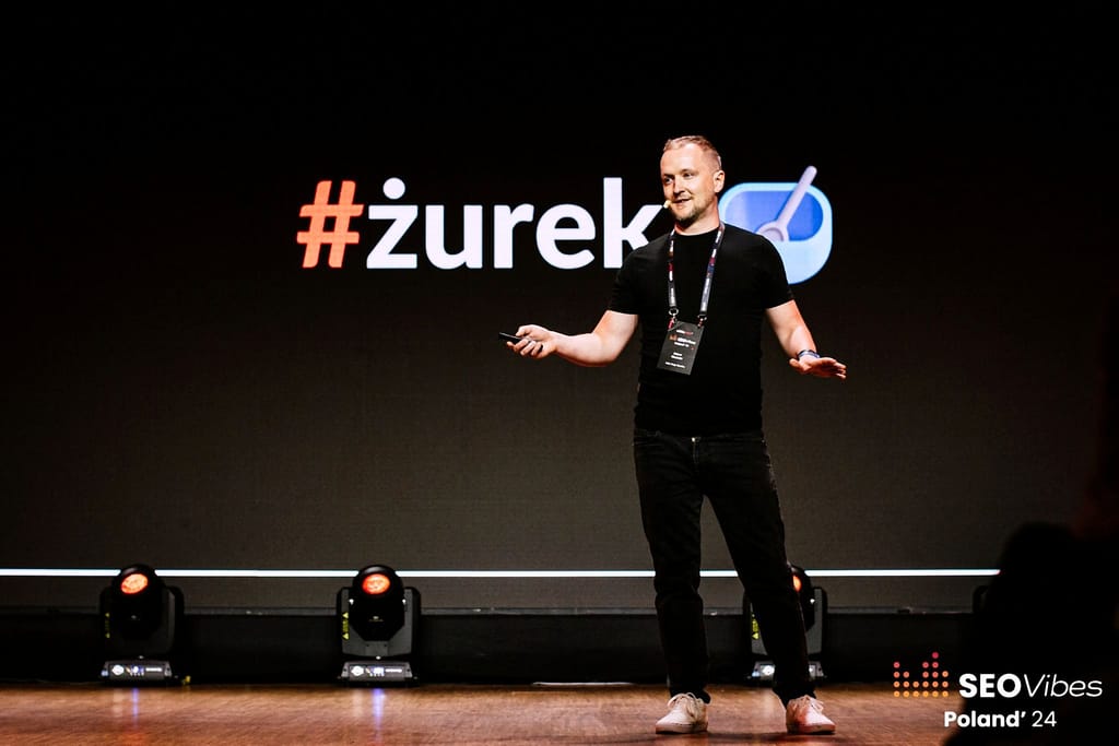 Robert Niechciał z rozłożonymi rękami na scenie głównej SEO Vibes Poland 2024, w tle slajd „#żurek”