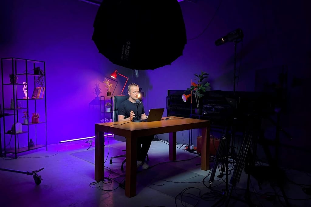 Robert Niechciał nagrywa przy biurku z laptopem i mikrofonem w studiu z fioletowym światłem
